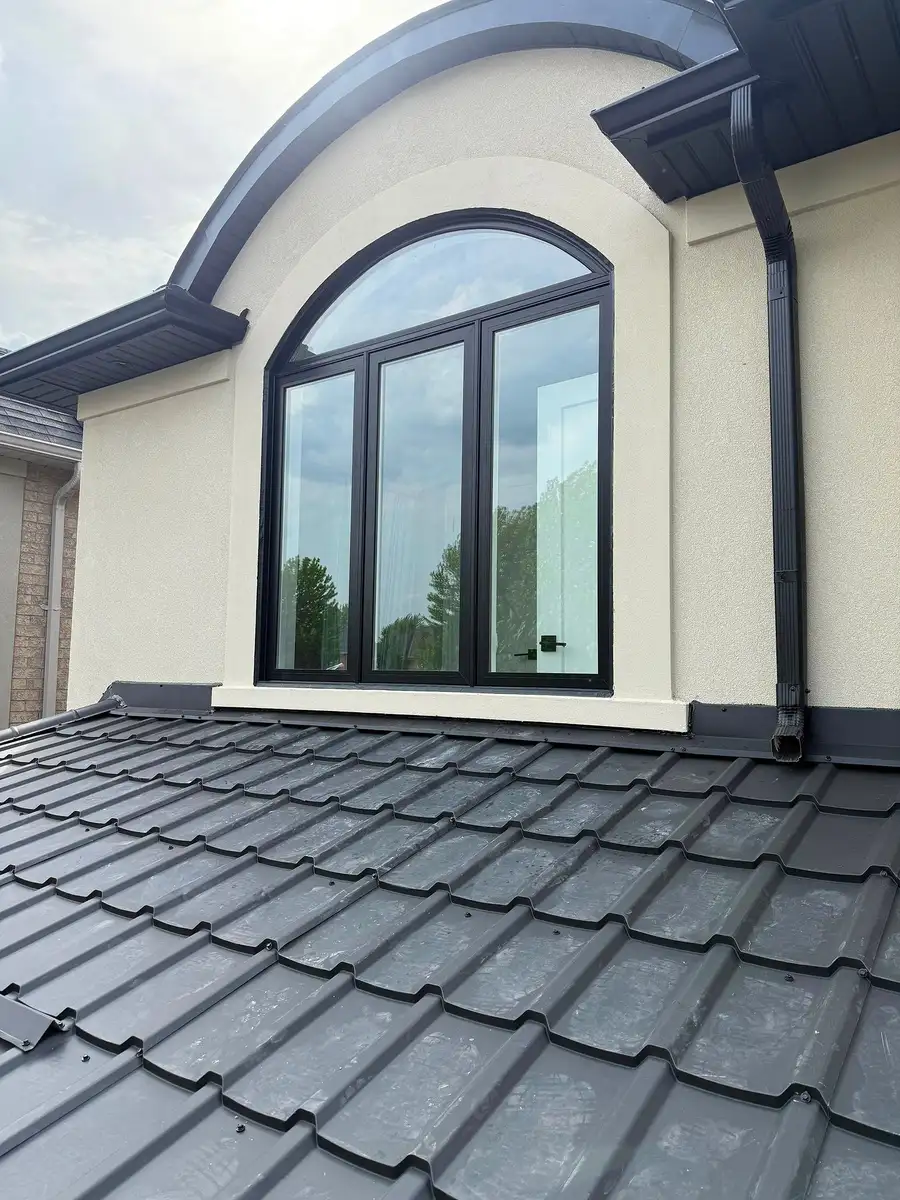 Black arched window with casement sashes, set in stucco above a metal-tile roof