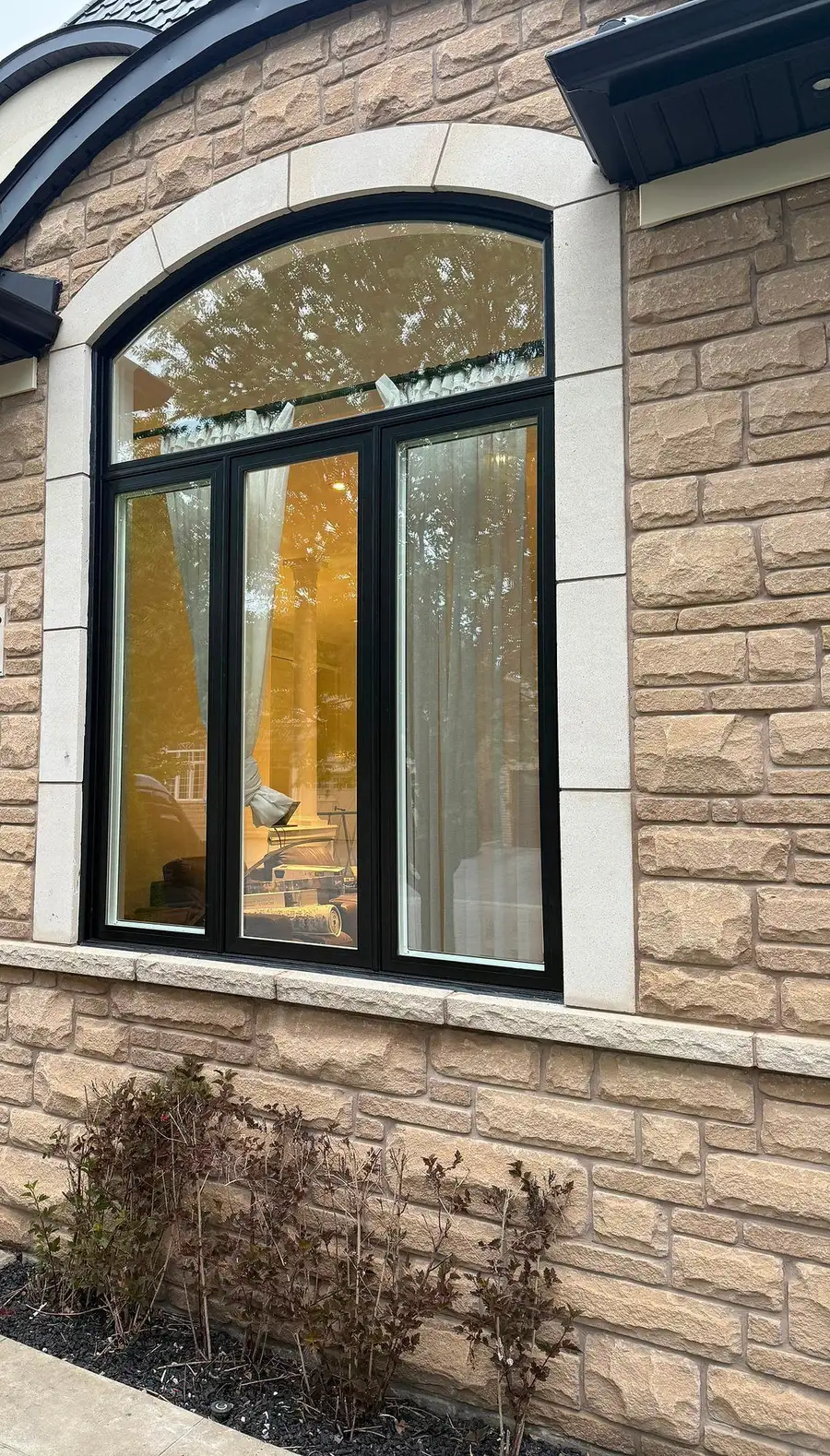 Large black arched window with casement sashes in a stone and stucco front