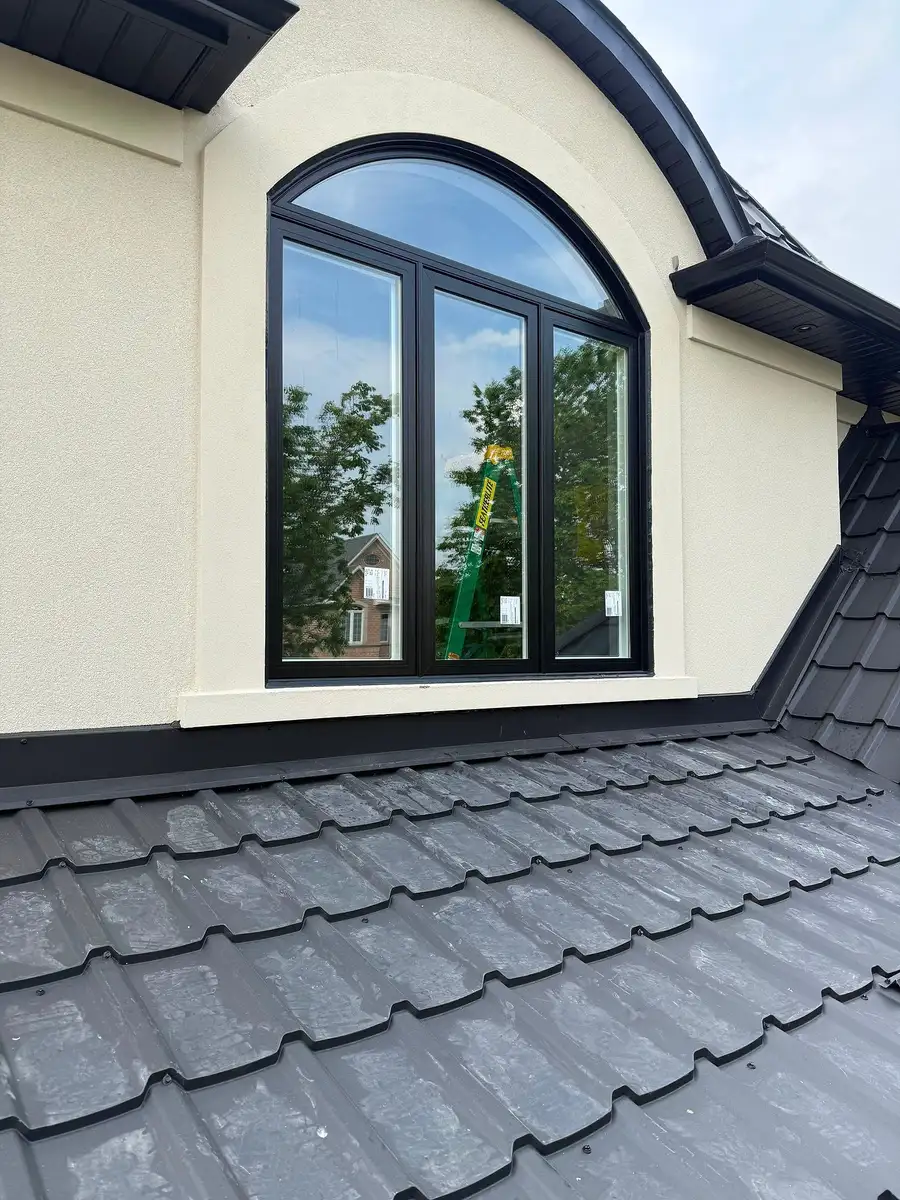 Black arched window in cream stucco under a dark metal-tile roof