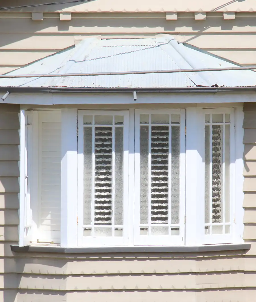 White bay window with three sections and interior shutters, under a metal roof on a clapboard house