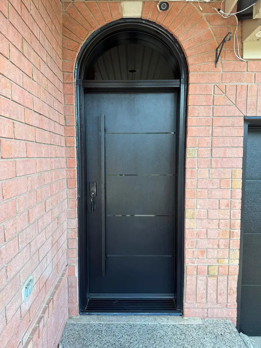 Black single entry door with a matching arched transom, fitted into an arched brick opening