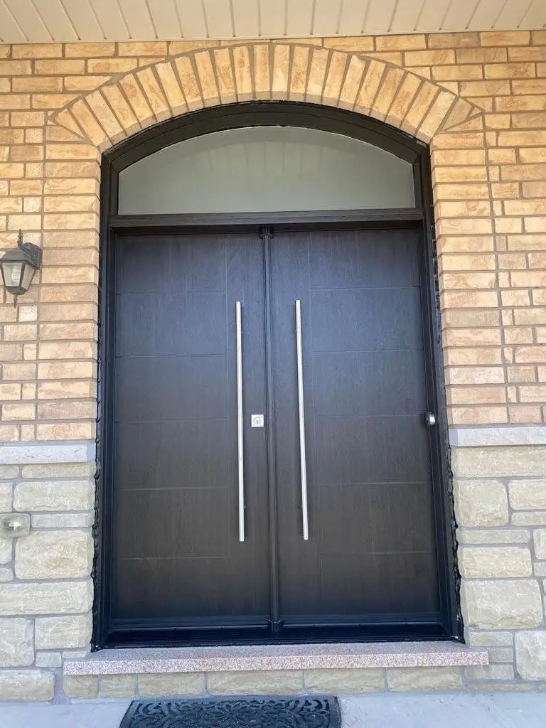 Black double entry door with long pulls under an arched transom, in a brick archway
