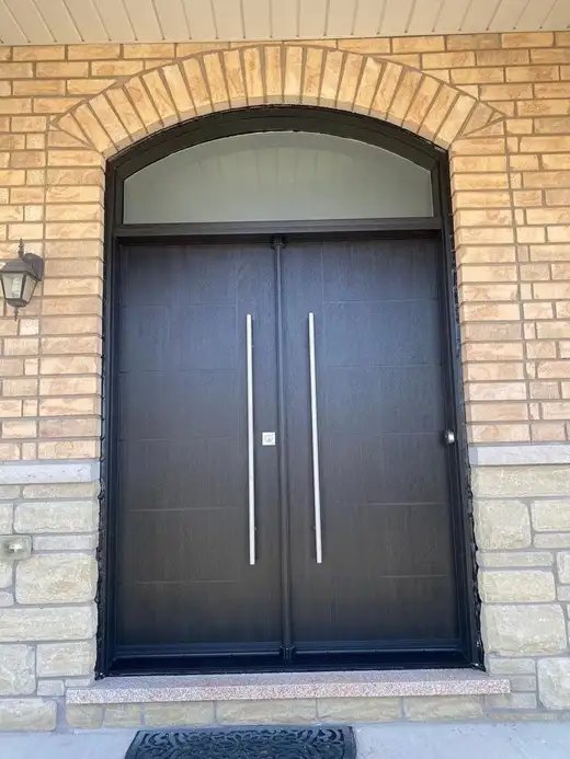 Black double entry door with long pulls under an arched transom, in a brick archway