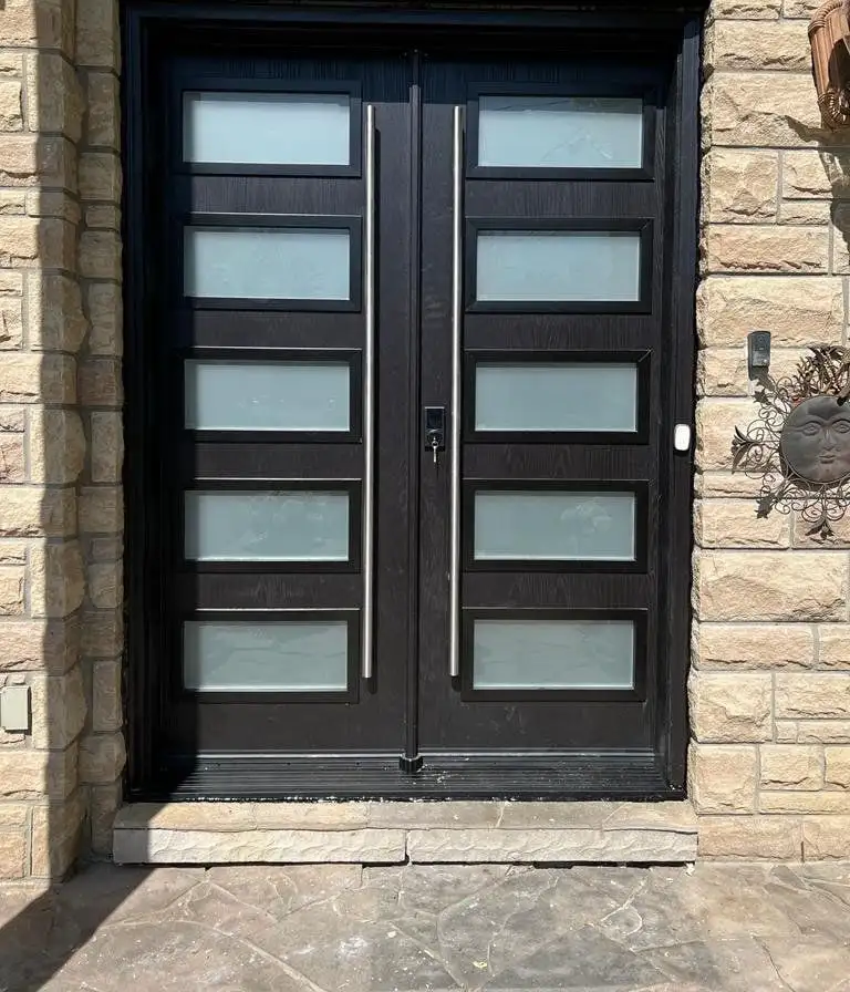 Black double entry door with stacked frosted glass lites and long stainless pulls, in a stone front