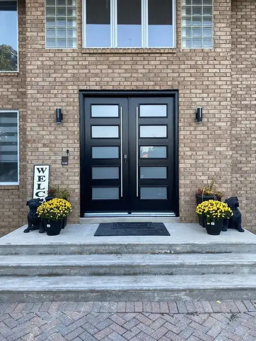 Black double entry door with frosted glass lites on a front porch with potted mums