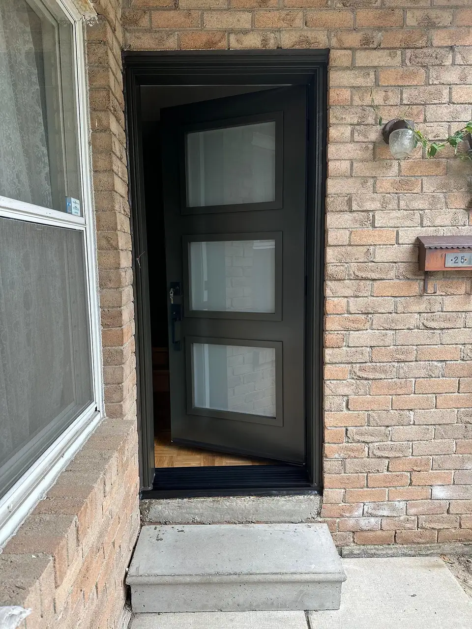 Black entry door with frosted glass lites beside a tall window, at the top of a short concrete step