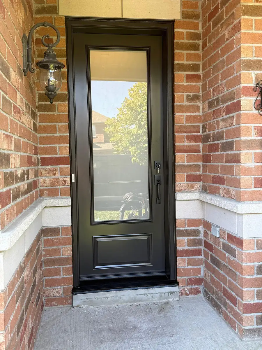 Black entry door with a full-length clear glass lite, in a red brick entrance with a coach lantern