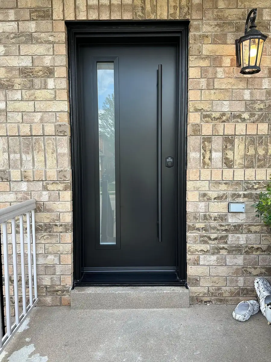 Black entry door with a narrow vertical glass lite and a long pull bar, in a stone and brick front