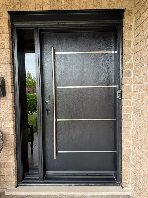 Black woodgrain entry door with a full-height glass sidelite, horizontal stainless bars and a long vertical pull