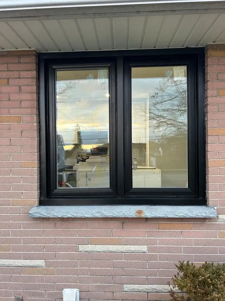 Black double casement window with a stone sill, in pink brick