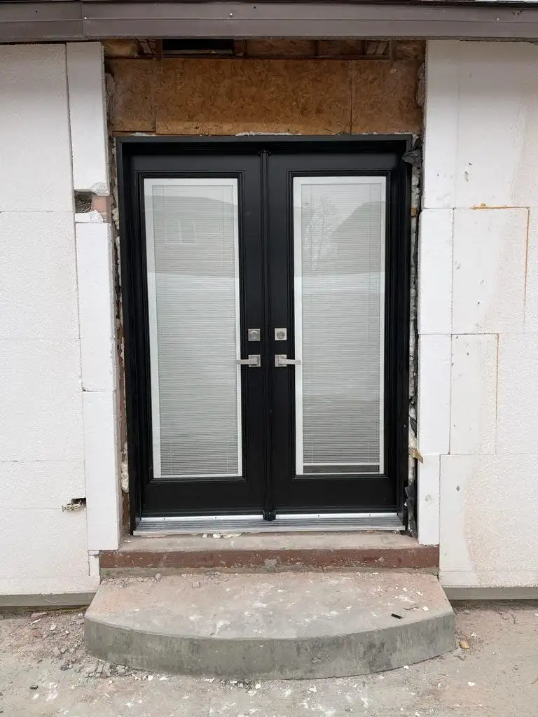 Black French doors with blinds between the glass, newly installed in a fresh masonry opening above concrete steps