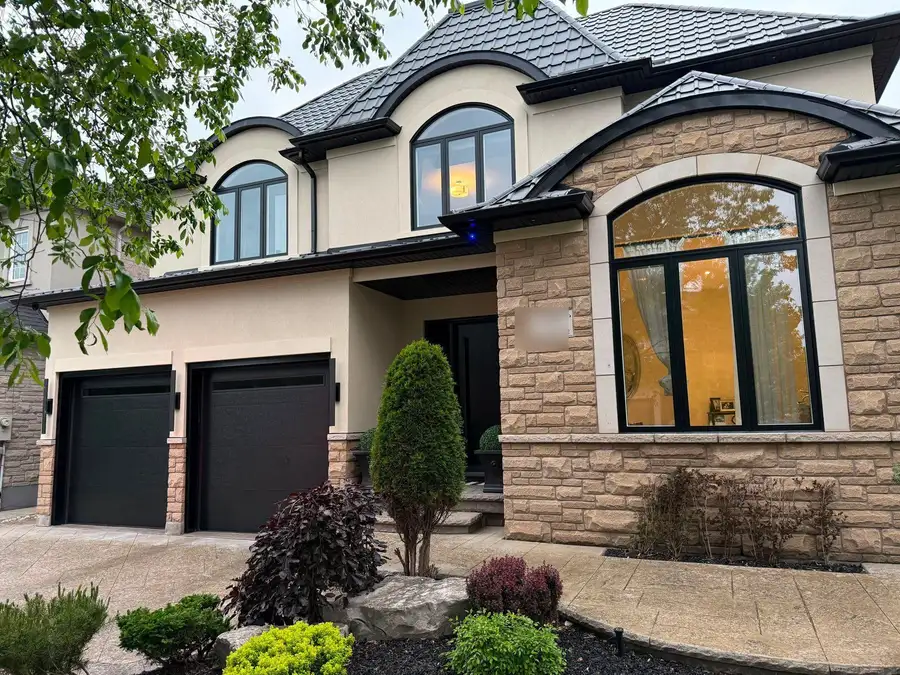 Two-storey stone and stucco house with black arched windows, two black garage doors and a black front door