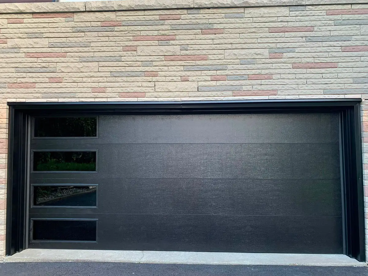 Wide black flush garage door with a column of glass lites at one side, in buff brick