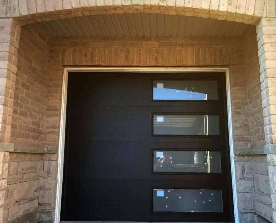 Black garage door with frosted glass lites, framed by a stone surround