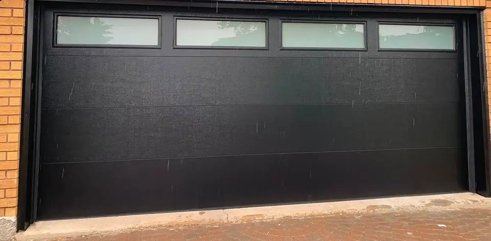 Black flush garage door with a row of frosted glass lites across the top section, in orange brick