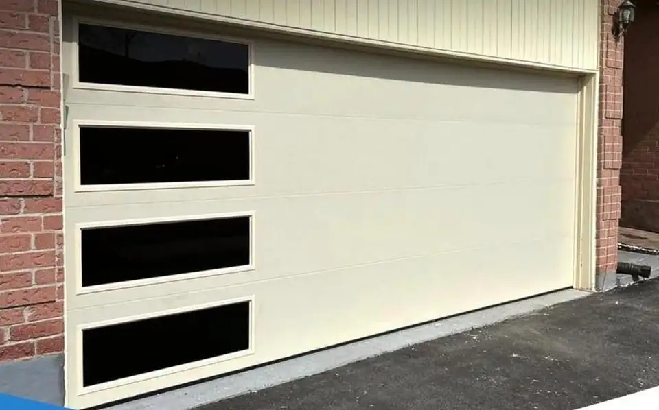 Wide cream garage door with a column of black-framed glass lites, beside red brick
