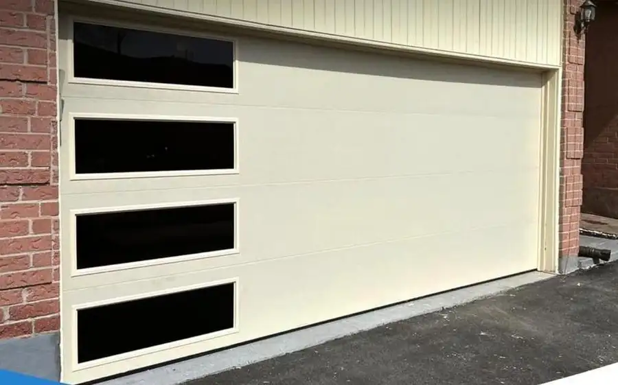 Wide cream garage door with a column of black-framed glass lites, beside red brick