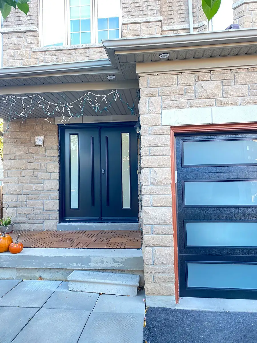 Full-view garage door with frosted glass panels in a black aluminium frame, next to a black double entry door
