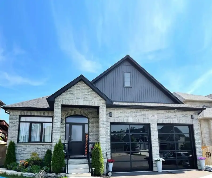 Stone bungalow with two black glass-lite garage doors and a dark front door, under a blue sky
