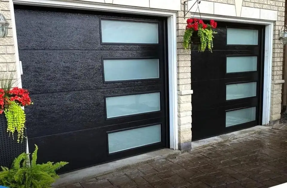 Two black garage doors with large frosted glass lites, beside hanging baskets of red flowers