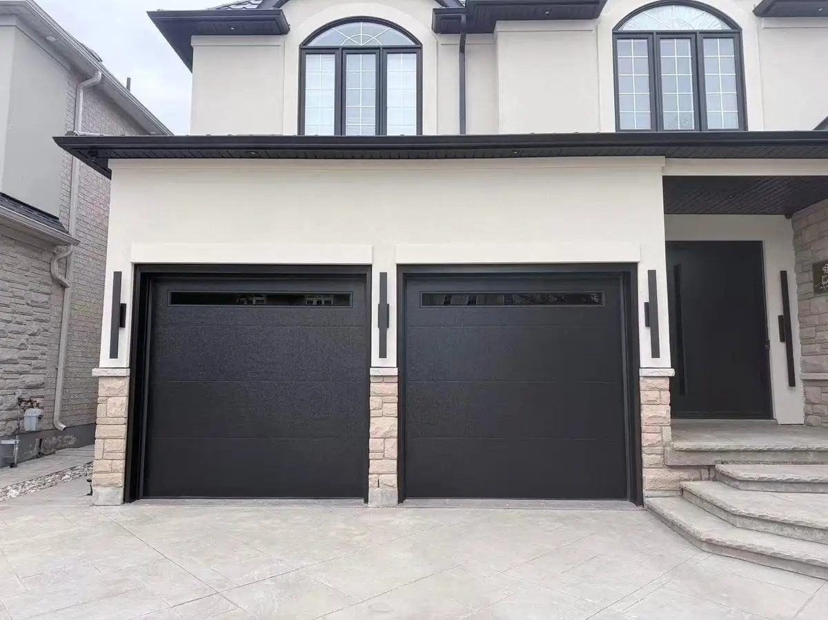 Two black flush garage doors with a slim row of lites, on a new white stucco house with arched windows