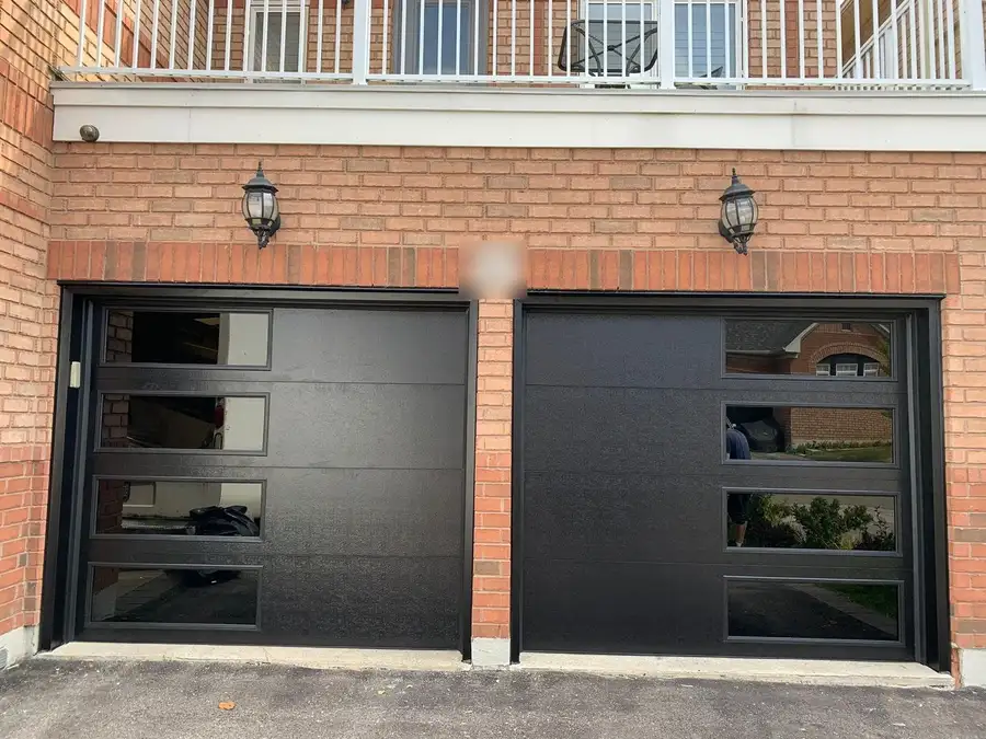 Two black flush garage doors with glass lites along one side, under a brick facade with coach lanterns