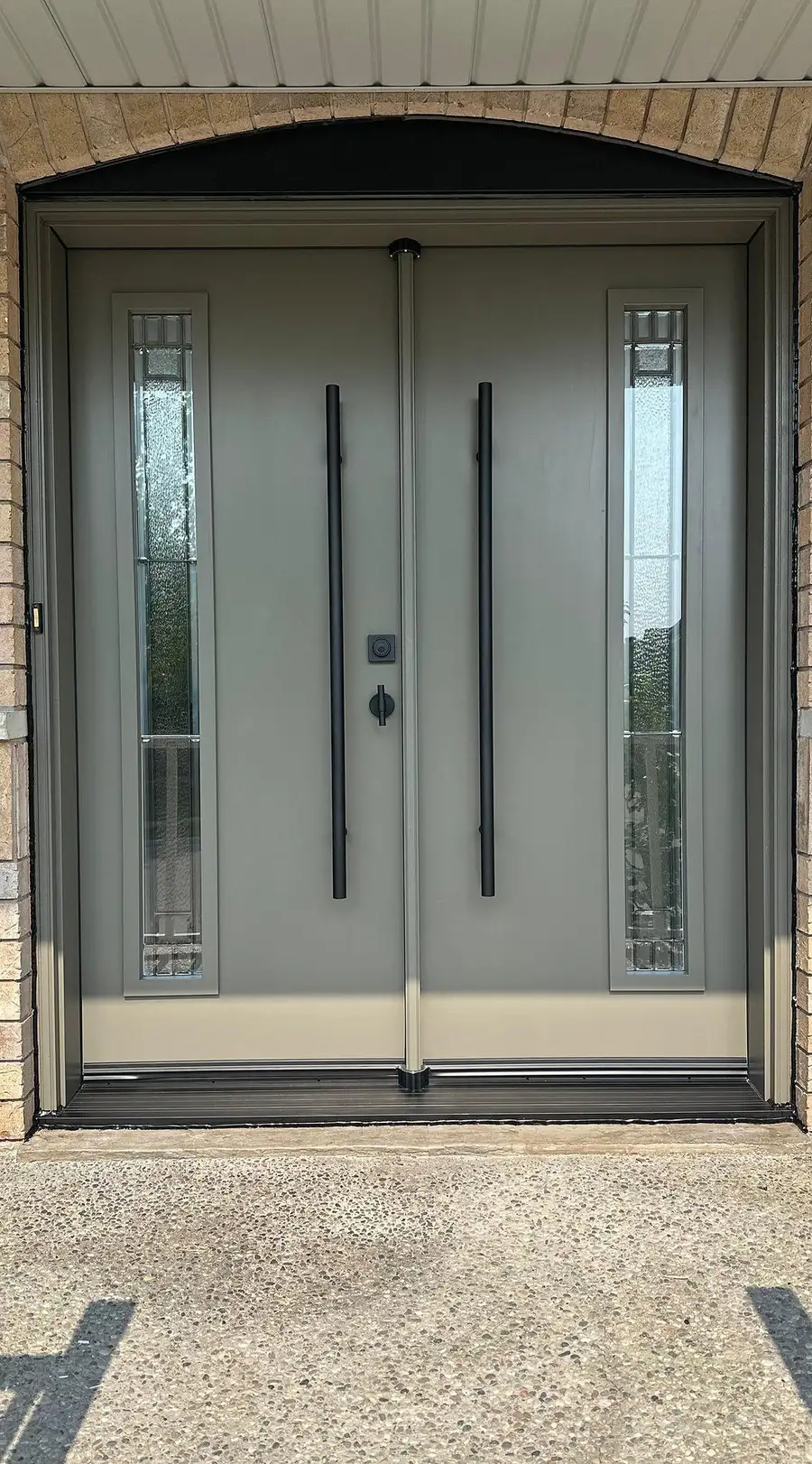 Grey double entry door with decorative glass inserts and two long black pull bars, under a brick arch