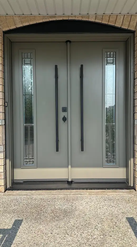 Grey double entry door with decorative glass inserts and two long black pull bars, under a brick arch