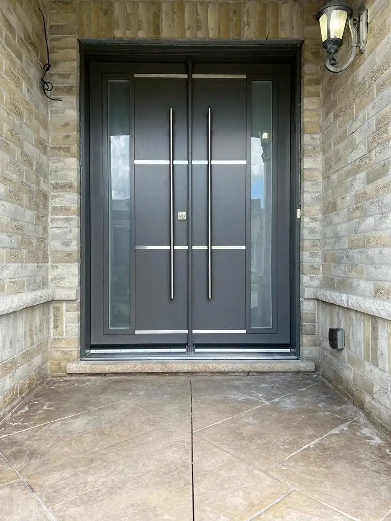 Charcoal double entry door with long vertical pulls and glass sidelites, in a stone porch