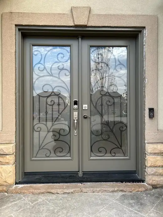 Grey double entry door with decorative wrought-iron glass in both leaves, in a stone entrance
