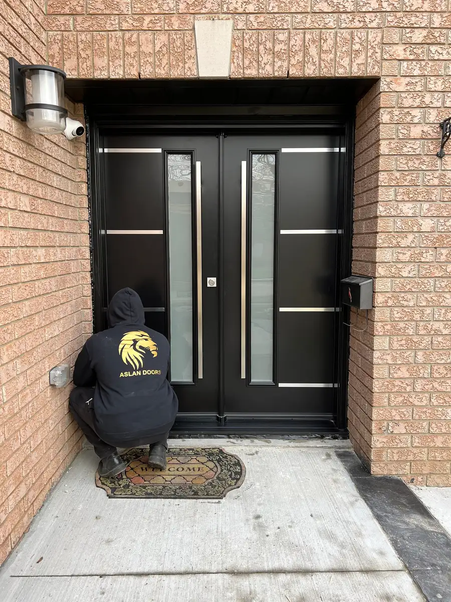 Aslan Doors installer in a branded black hoodie adjusting a newly installed black double entry door