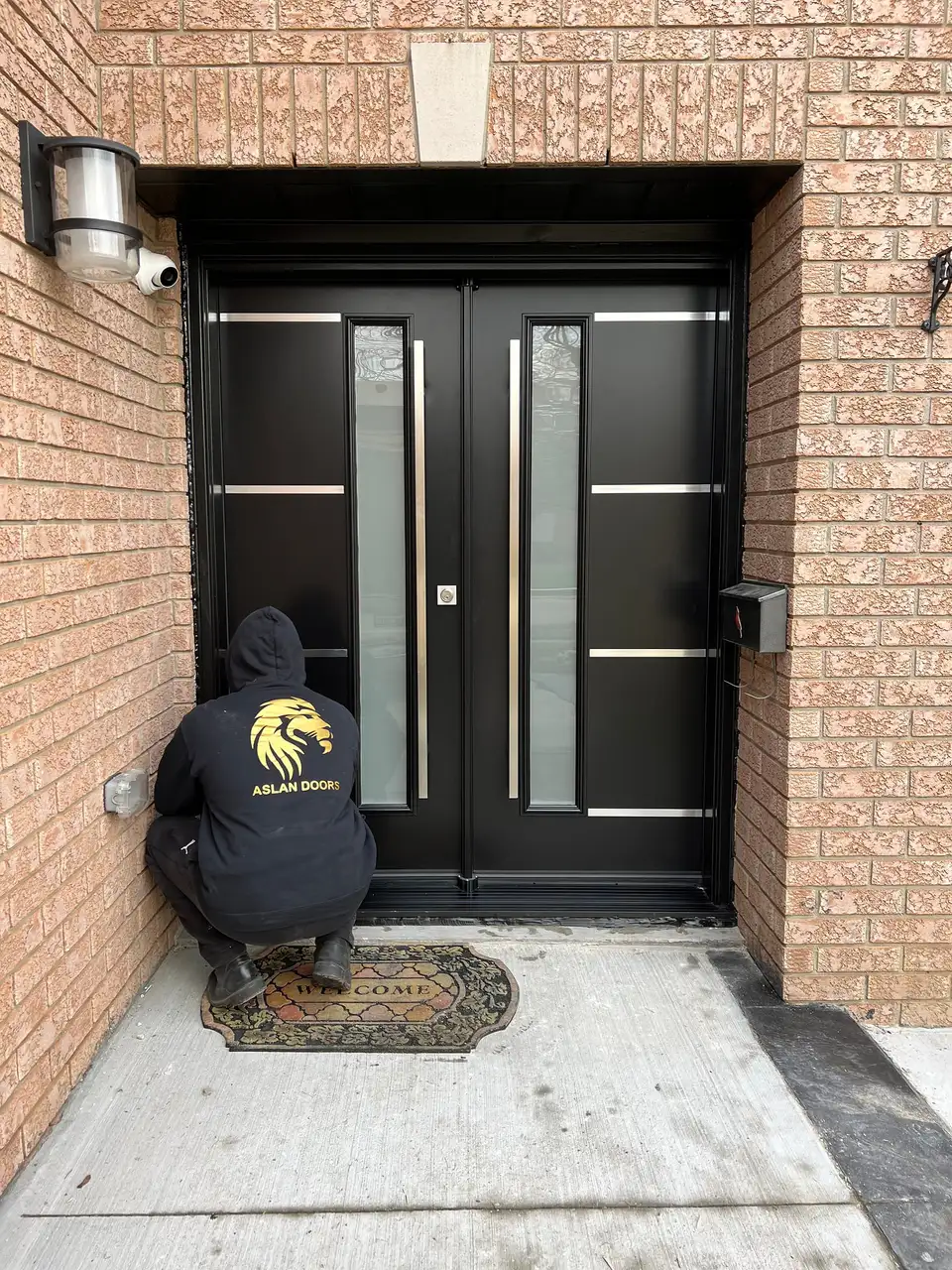 Aslan Doors installer in a branded black hoodie adjusting a newly installed black double entry door