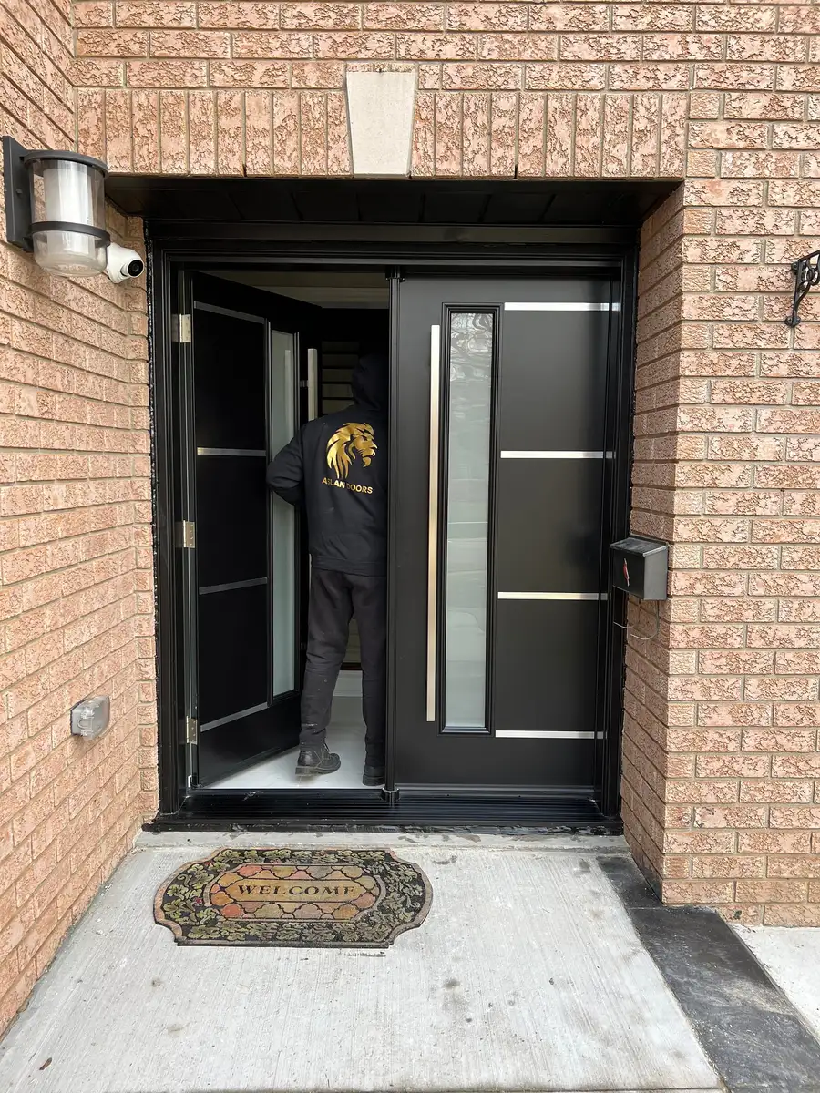Black double entry door standing open during installation, an Aslan Doors installer working inside