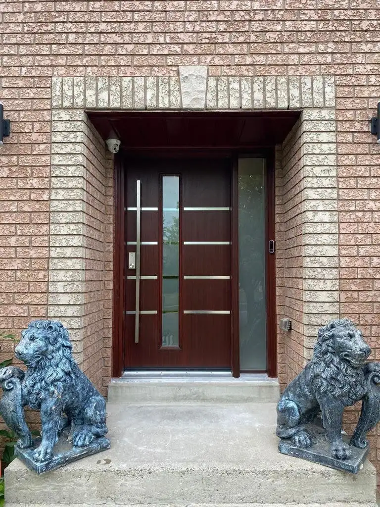 Mahogany-finish entry door with stainless bars, flanked by two stone lion statues at the top of the front steps