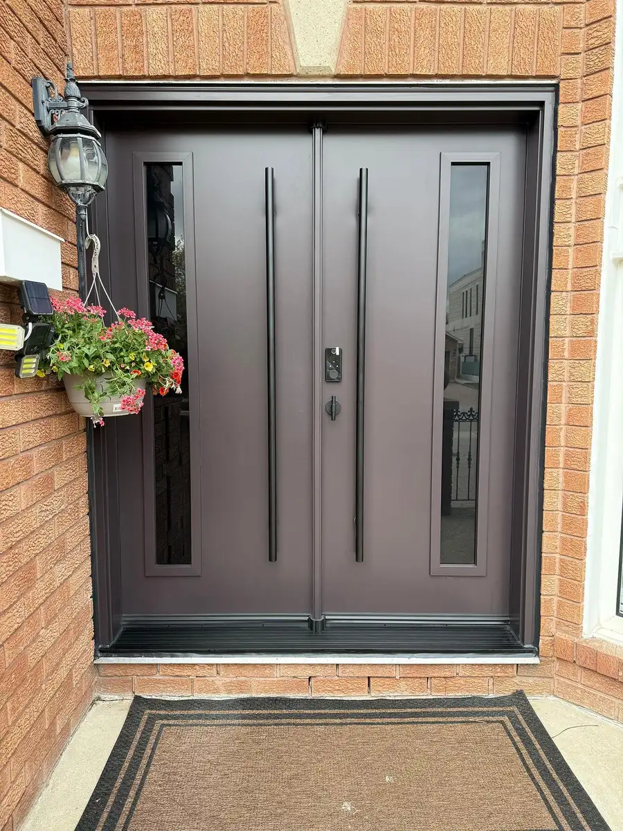 Dark double entry door with dual pull bars and slim vertical glass inserts, in red brick with a hanging flower basket