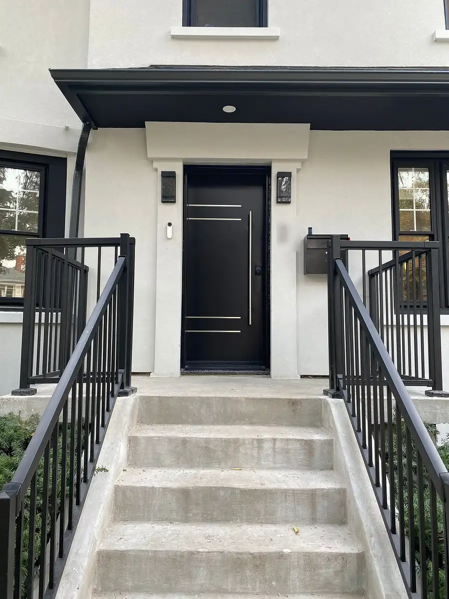 Black modern entry door with stainless bars at the top of concrete steps with black railings, on a white stucco house