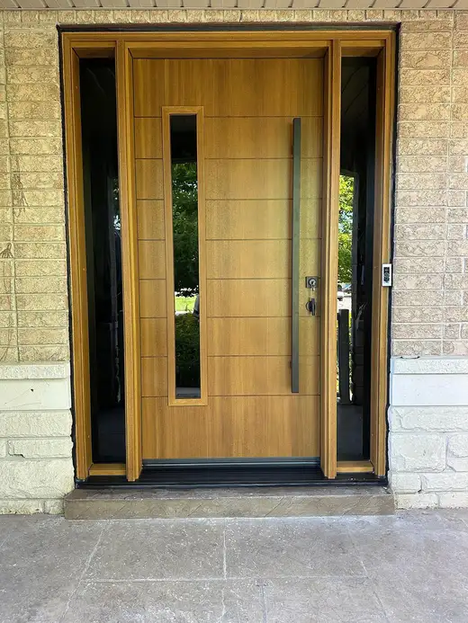 Light oak woodgrain entry door with a narrow glass insert, long pull and matching glass sidelites