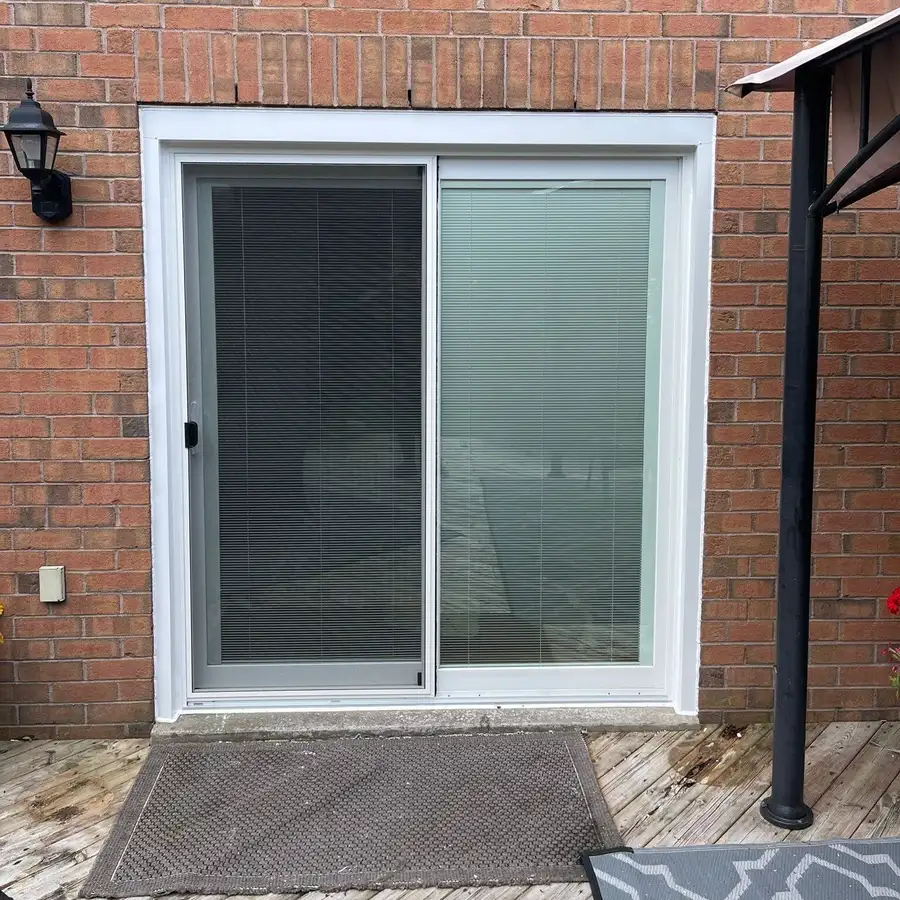 White sliding patio door with blinds between the glass, set in red brick above a wooden deck