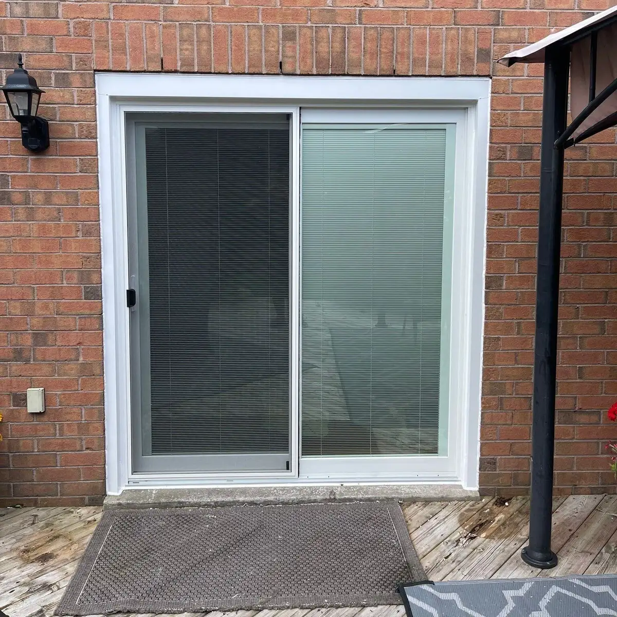 White sliding patio door with blinds between the glass, set in red brick above a wooden deck