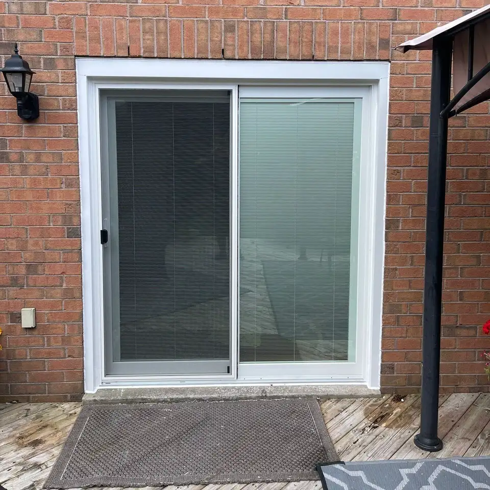 White sliding patio door with blinds between the glass, set in red brick above a wooden deck