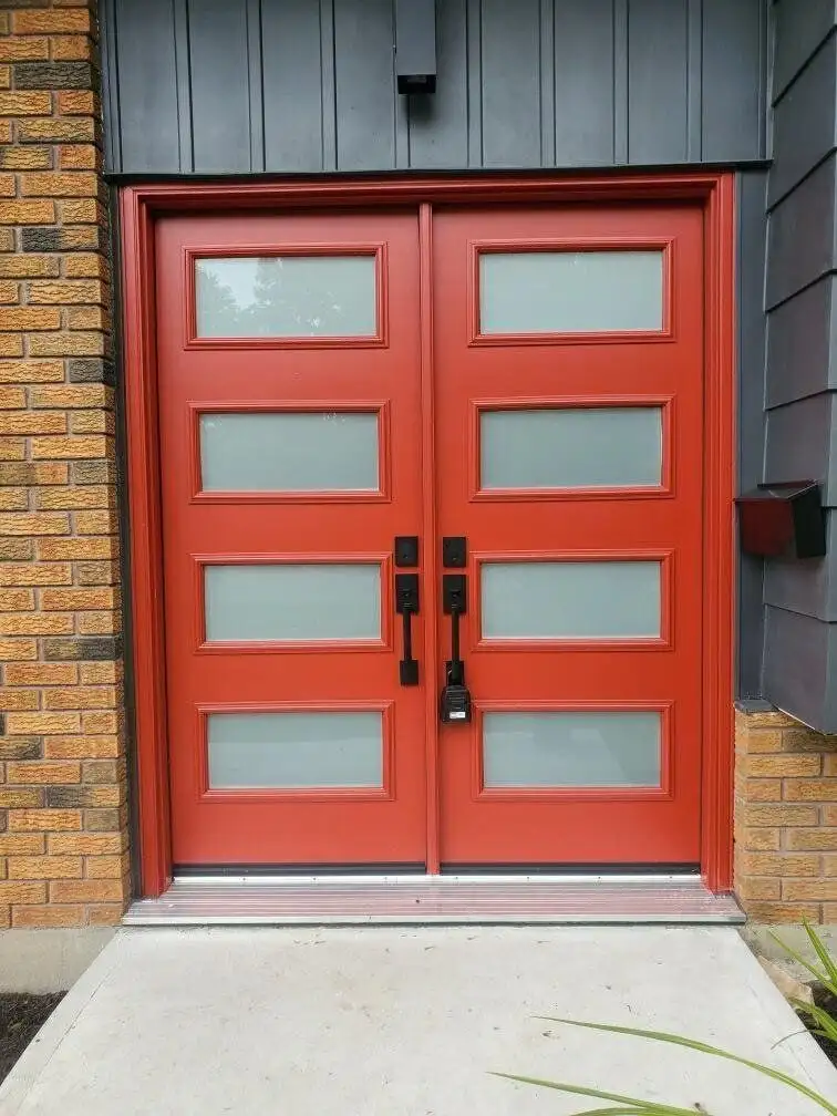 Red double entry door with frosted glass lites and black hardware, against dark board-and-batten siding