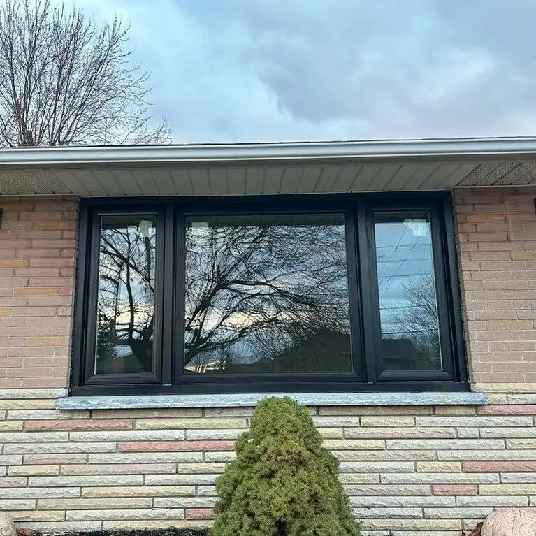 Black three-lite window with a wide fixed centre pane between two casements, in brick above a stone sill