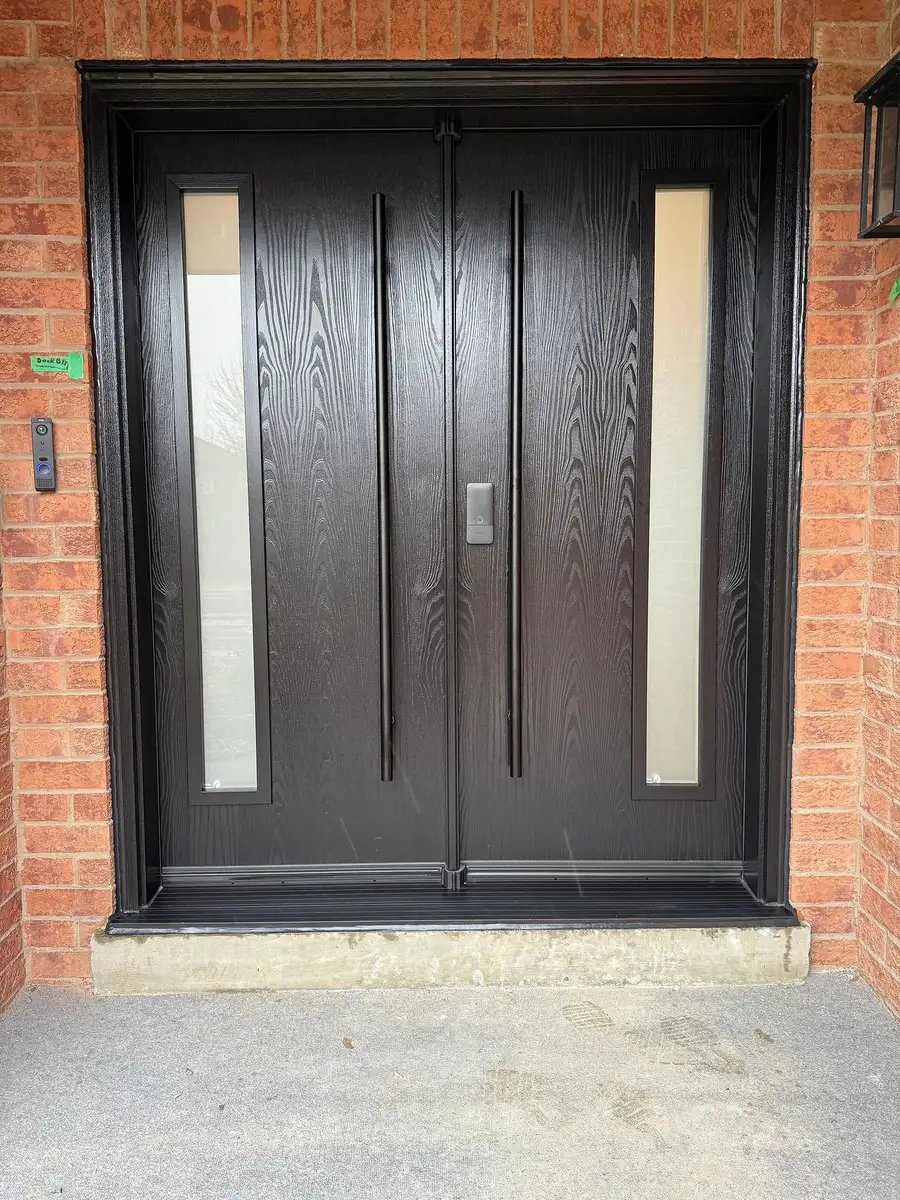 Dark woodgrain double entry door with slim frosted glass inserts and two long vertical pull bars, set in red brick